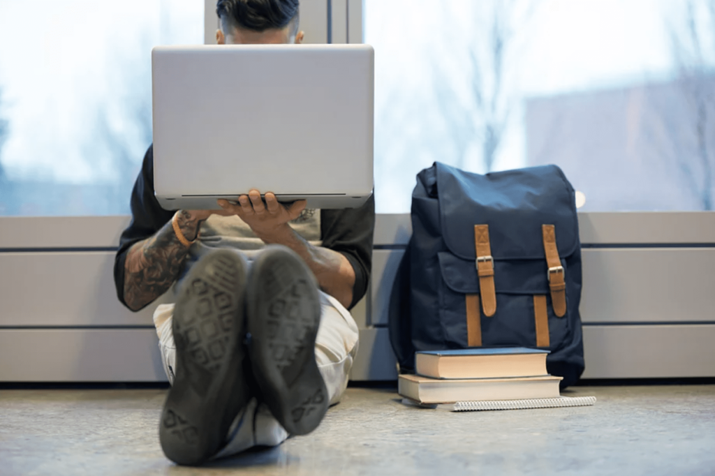 News and Updates Student sitting on floor with laptop, backpack and books
