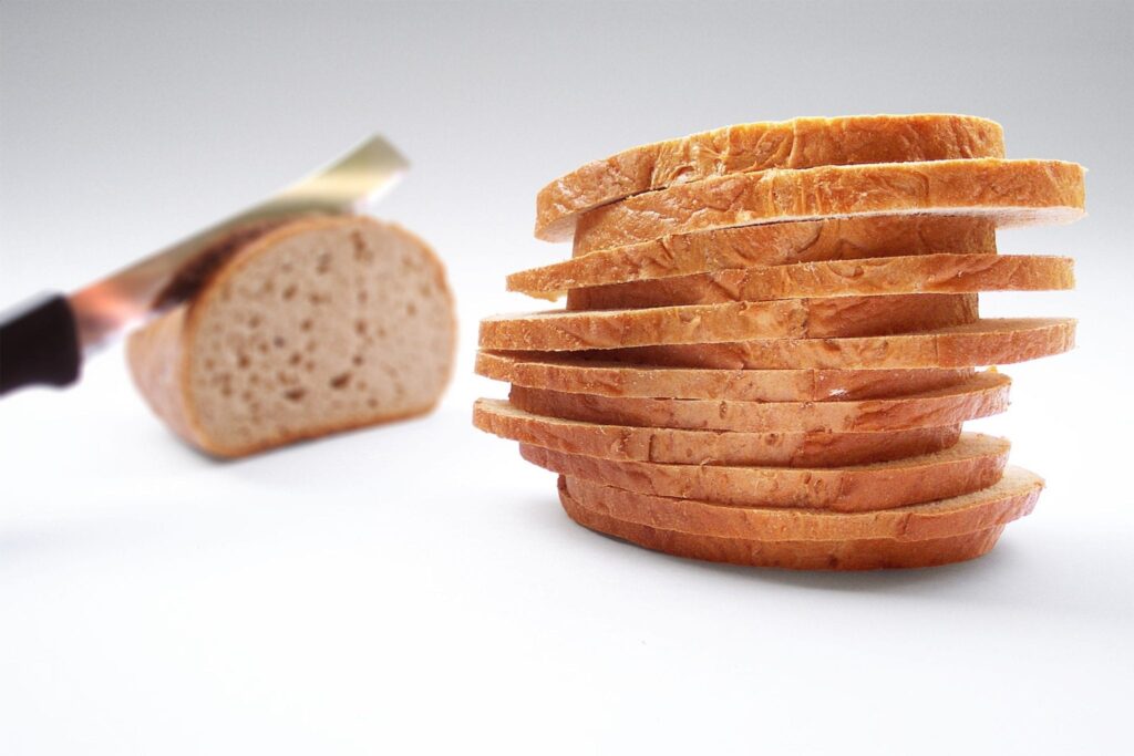 knife cutting into a loaf of bread next to a stack of slices