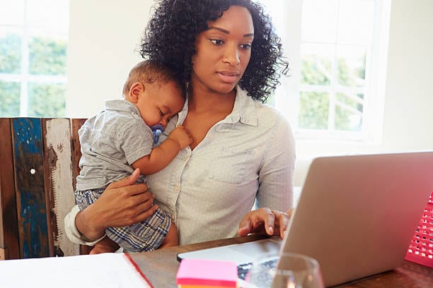 woman holding a sleeping infant working on a computer