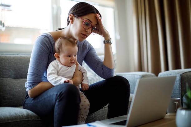 woman holding awake infant frustratedly staring at laptop screen
