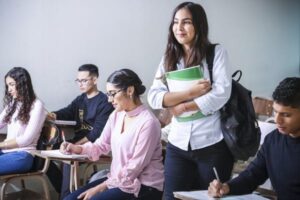 A student walks into the classroom while students at desks take notes